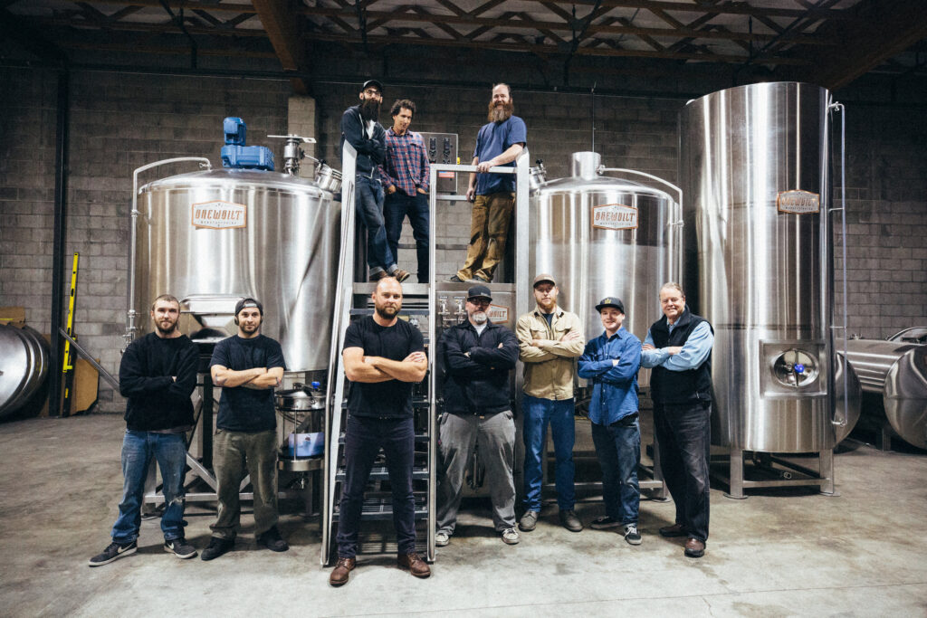staff posing in front of a brewing  machine