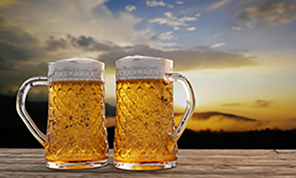 2 beer mugs full of beer in front of a sunset