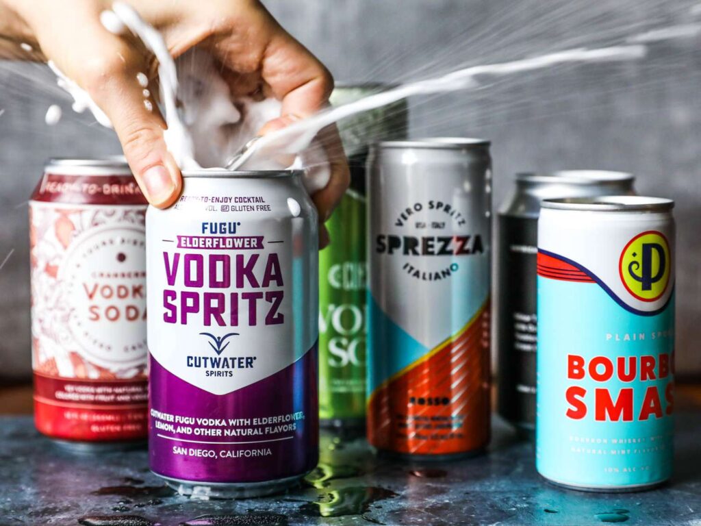 canned cocktail cans with one being opened and exploding with spray