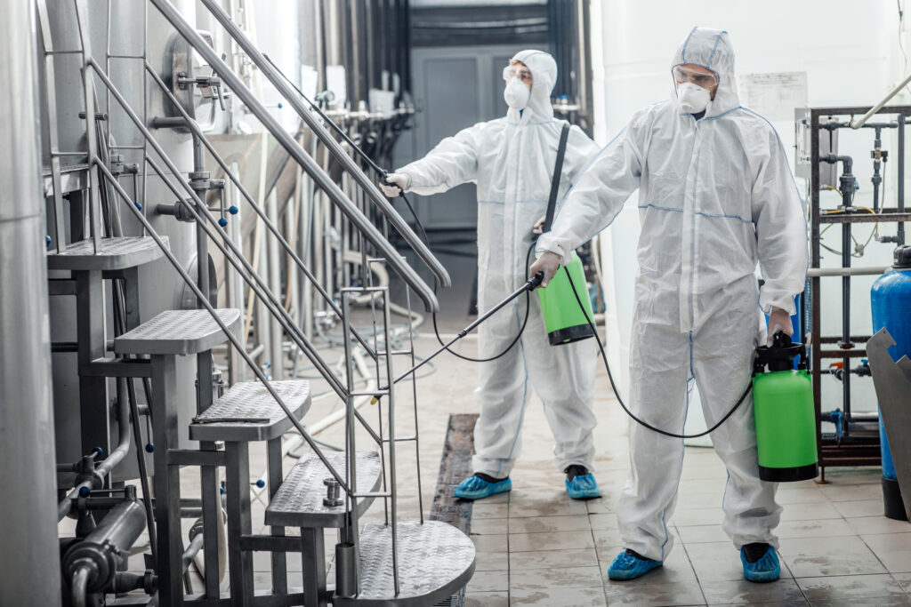 two people in hazard suits spraying down the production facility of a brewery or distillery
