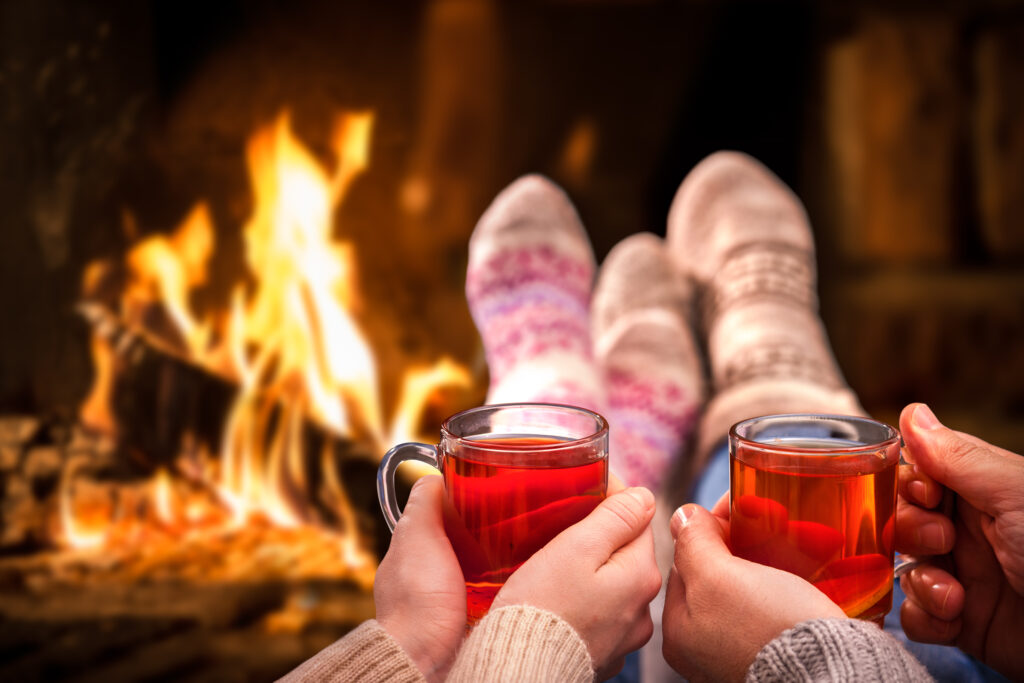 two people with their feet up in front of a fire each holding a cocktail