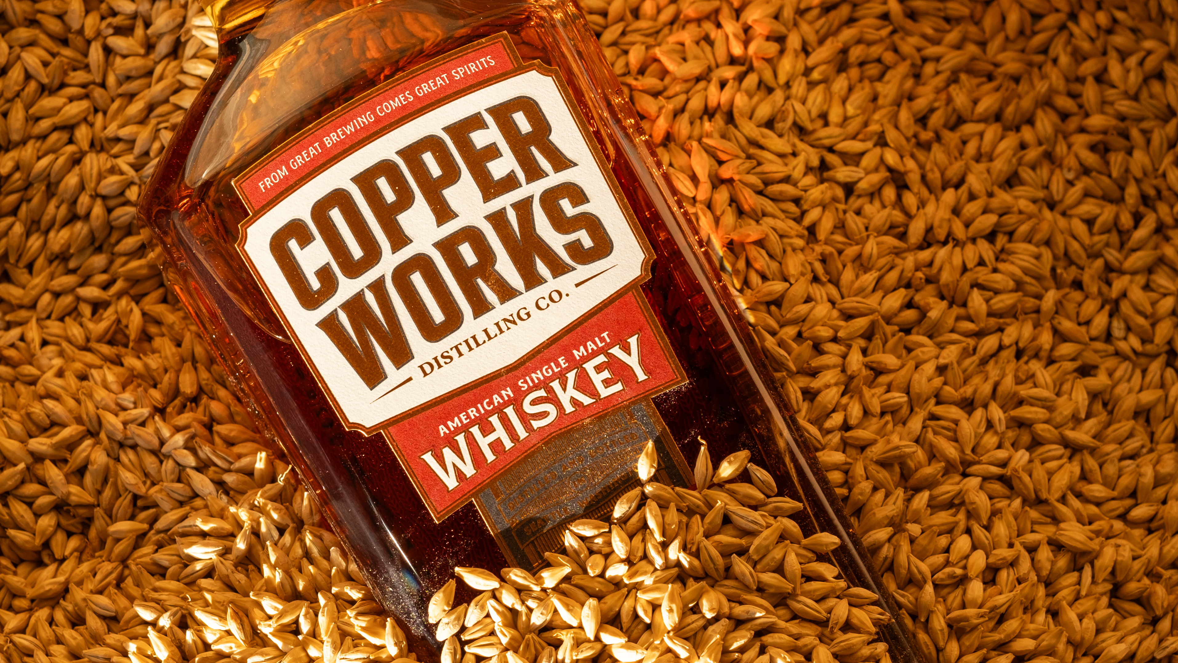 A bottle labled Copper Works distilling co laying in a bed of barley