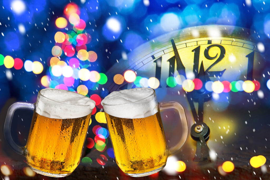 two beer mugs clinking together in front of a clock about to turn midnight on New Years Eve