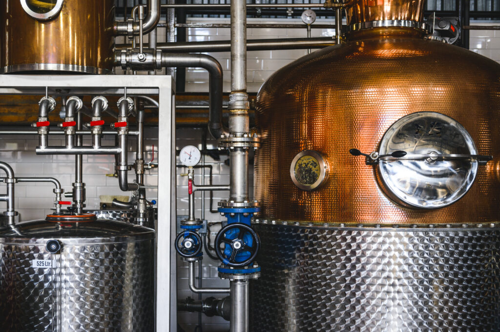 photo shows a copper still next to mash tanks in a distillery or brewery