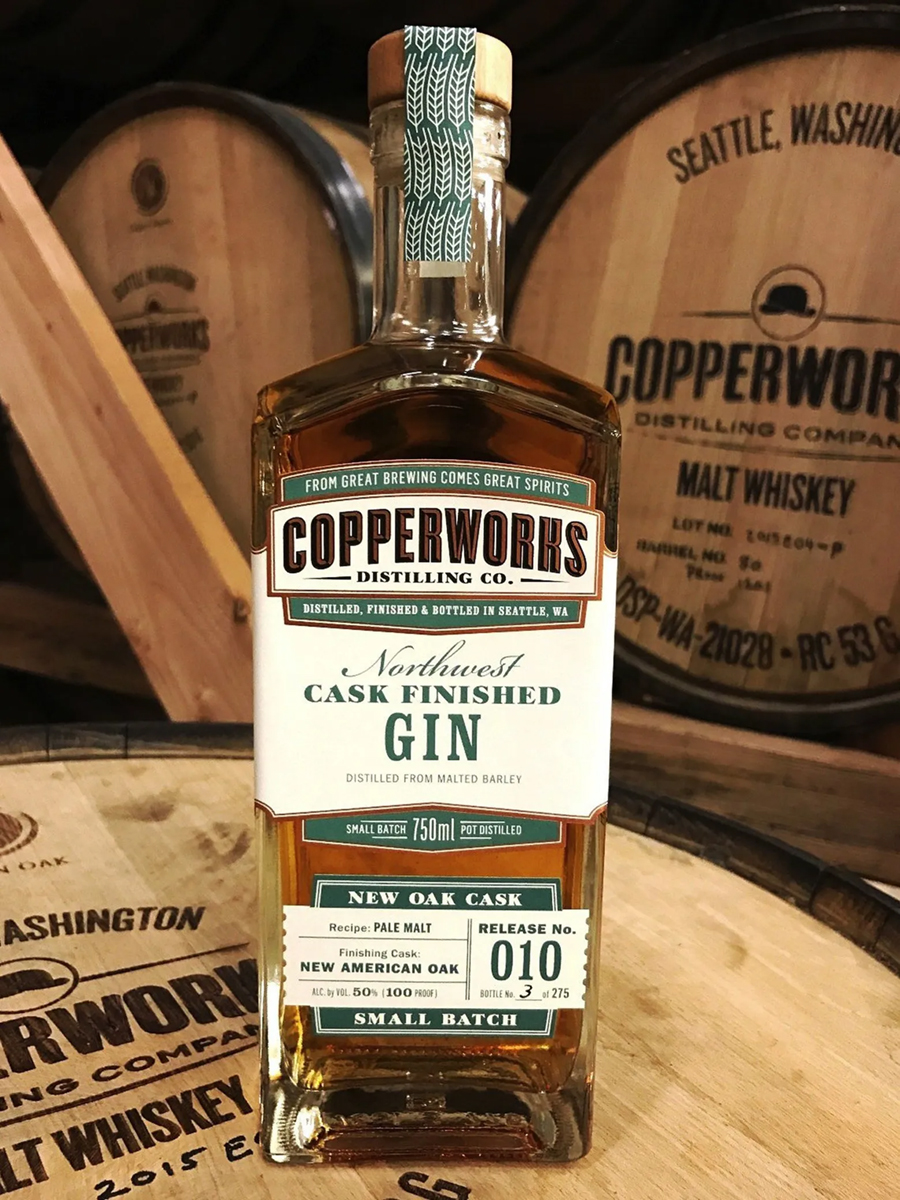 A COPPERWORKS GIN BOTTLE IN FRONT OF COPPERWORKS BARRELS